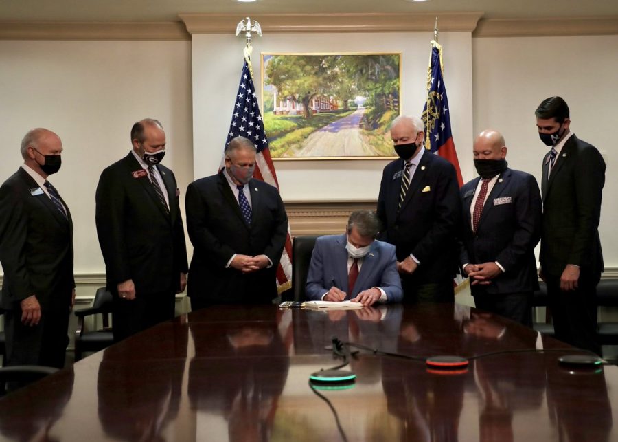Georgia Gov. Brian Kemp signs a bill targeting minority voters in front of a painting of a plantation that held slaves.
