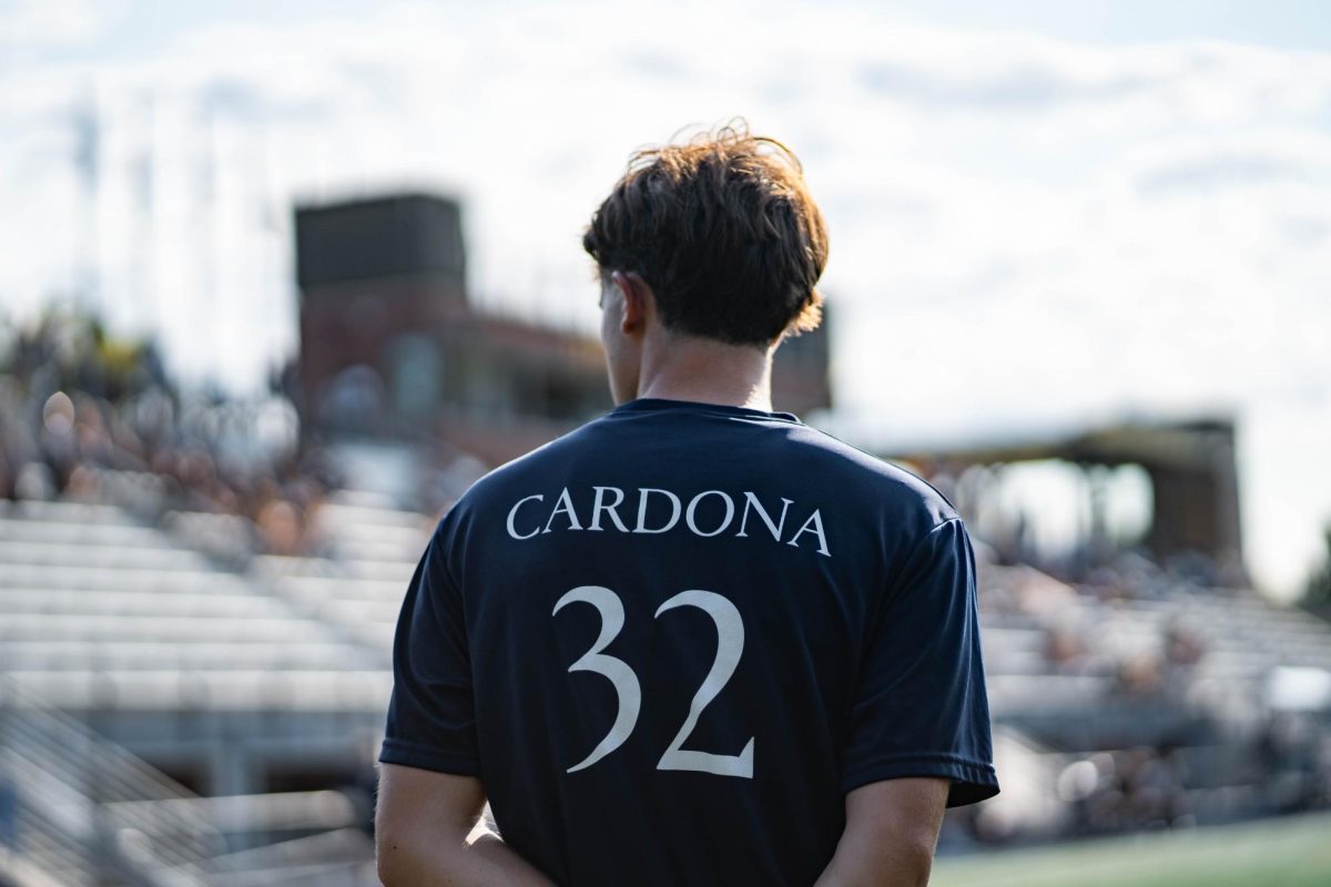 Quinnipiac men's soccer dawns navy dri-fit tees with white lettering, “WE’RE WITH YOU NICK” on the front and Cardona’s surname and number, 32 on the back.
